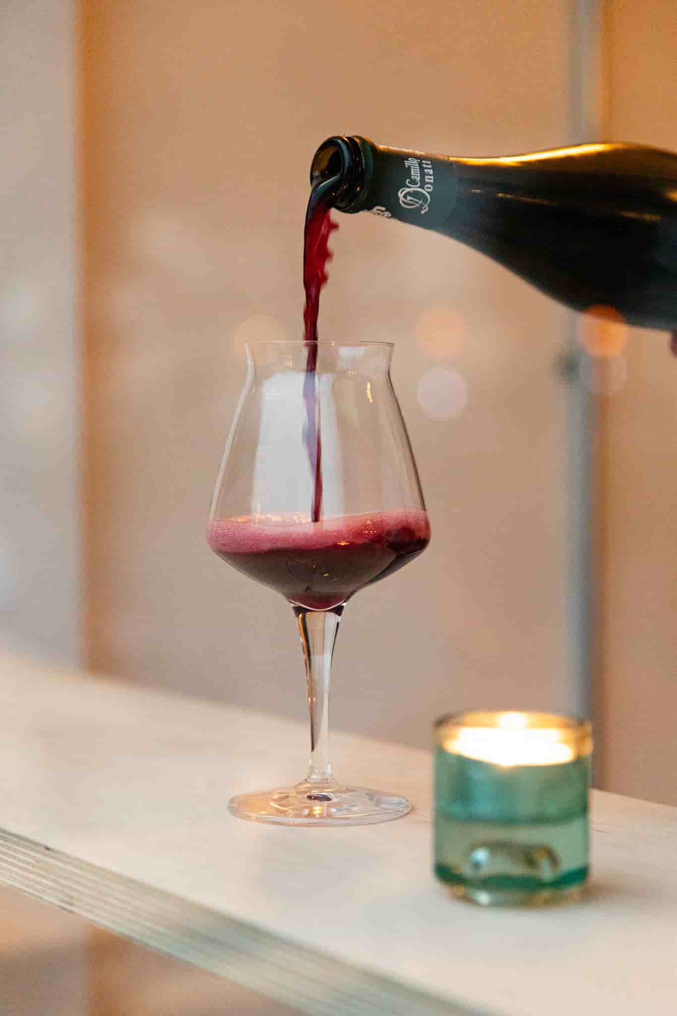 Red wine being poured into classy glass by Ellen Richardson